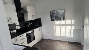 A modern kitchen with white cabinets, black countertops, and a herringbone-patterned floor.