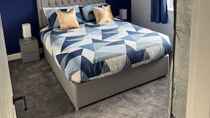 A bedroom with a bed, a nightstand, a lamp, and a window with curtains.