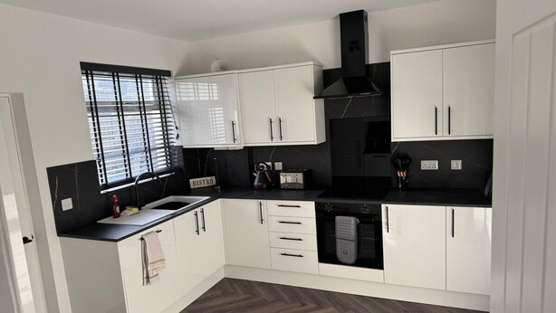 A modern kitchen with white cabinets, a black countertop, and a herringbone wood floor.