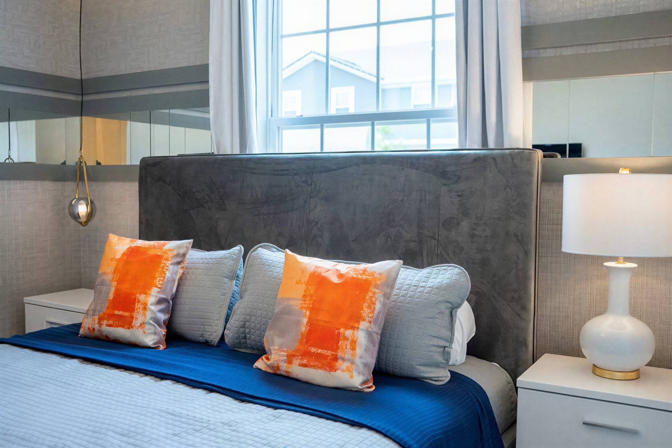 A hotel room with a large bed, a nightstand, a lamp, and a window with a view of a building.