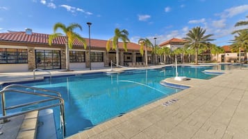 Una piscina con agua cristalina azul, rodeada de palmeras y un edificio con techo de tejas.