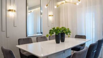 Un salón de conferencias con una mesa blanca, seis sillas, dos plantas en macetas, un espejo grande e iluminación instalada en la pared.