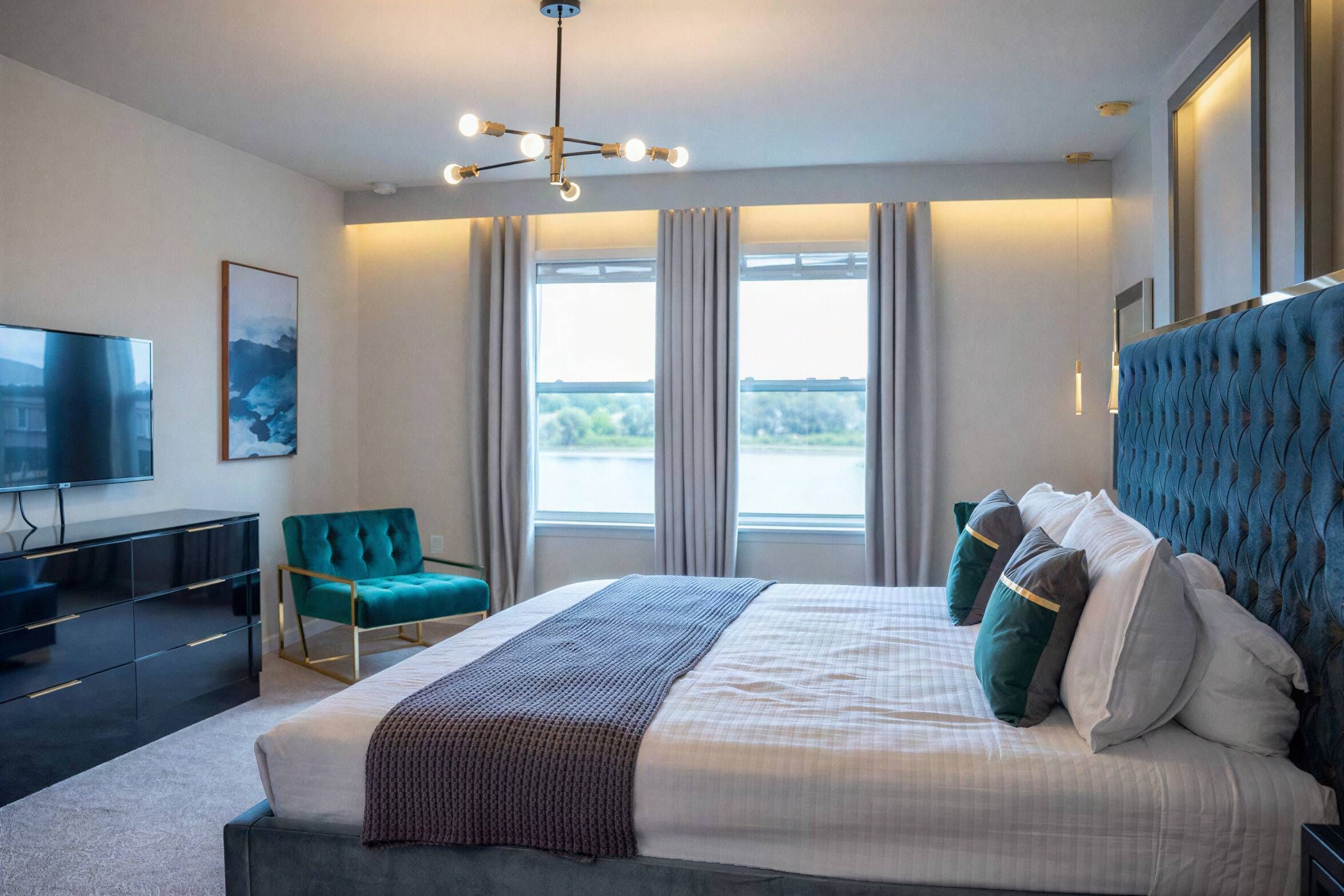 A modern bedroom with a large bed, a television, and a view of the outdoors through the windows.