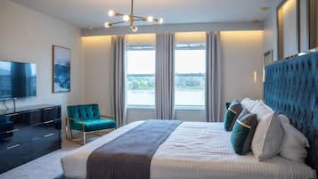 Un dormitorio moderno con una cama grande, un televisor y vistas al exterior a través de las ventanas.