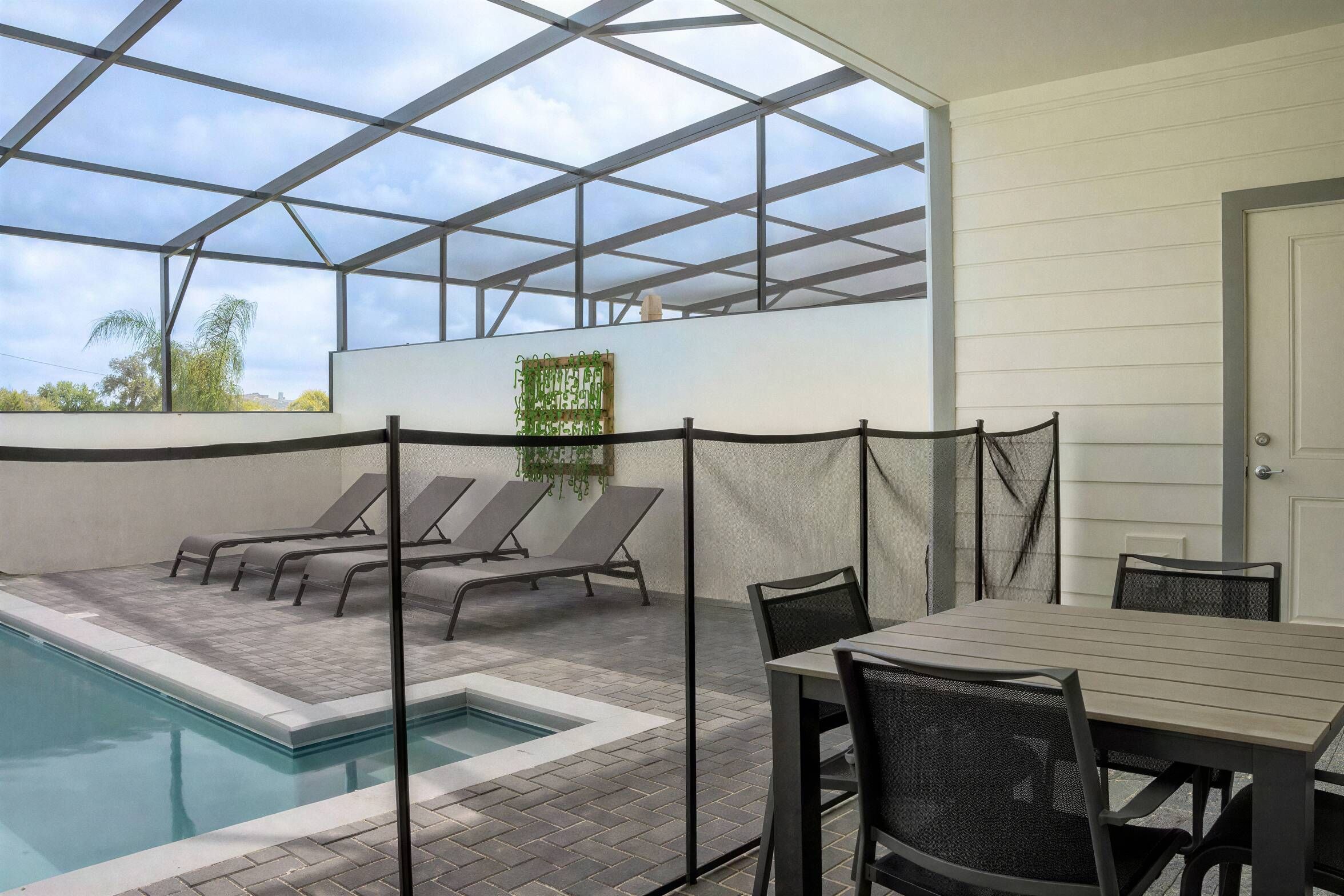 Un espace piscine aménagé avec des chaises longues et une table, le tout protégé par une structure de toit en verre.