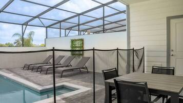 Zona de piscina con sillones de descanso y una mesa, rodeada por una estructura de techo de cristal.