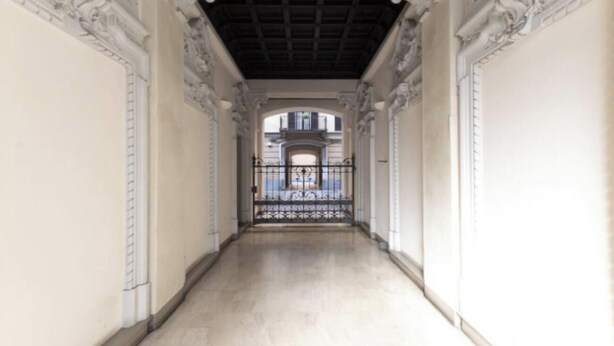 A corridor with ornate white walls and a black metal gate at the end. - Elegant Loft in the Heart of Milan – Spacious and Stylish
 (Milano)