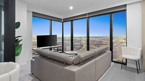 A modern living room with a large sectional sofa, a flat-screen TV, and a city view through large windows.