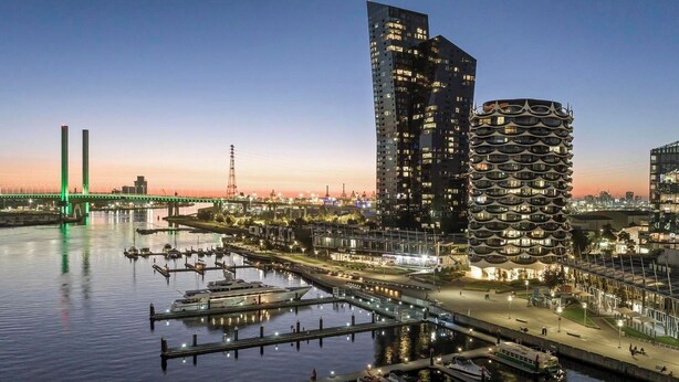 A waterfront cityscape with modern architecture, including a distinctive curved building and a tall skyscraper.