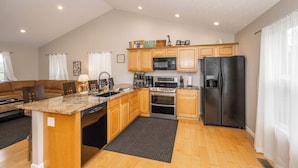 A kitchen with wooden cabinets, a granite countertop, stainless steel appliances, and a dining area with a brown leather couch.