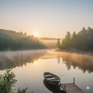 Un lac paisible, avec un quai en bois et un petit bateau, entouré d’arbres et de brume.