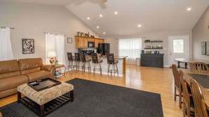 A spacious living room with a brown leather sofa, a coffee table, and a dining area with wooden chairs and a table.
