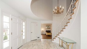 A spacious hallway with a marble floor, a glass console table, and a grand staircase with a decorative railing. - Tallen Manor & Retreat (Hamilton)