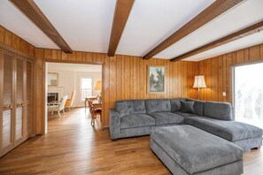 A living room with wooden paneling, a sectional sofa, and a dining area with a table and chairs. - Tallen Manor & Retreat (Hamilton)