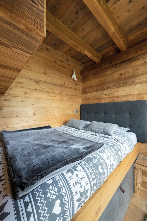 A bedroom with a wooden ceiling and walls, a bed with patterned bedding, and a headboard.