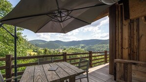 Eine Holzterrasse mit Tisch und Stühlen, einem Sonnenschirm und Blick auf eine gebirgige Landschaft.