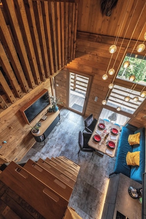 A high-ceilinged wooden interior with a dining area, seating, and a television. - Chalet "Le Cocoonid" - Bain Nordique - Sauna (Ventron)