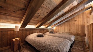 Ein Zimmer mit Holzboden, zwei Betten, einem Nachttisch und einer Lampe.