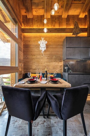 Un intérieur en bois avec une table à manger dressée pour deux personnes, une horloge et un petit sapin de Noël.