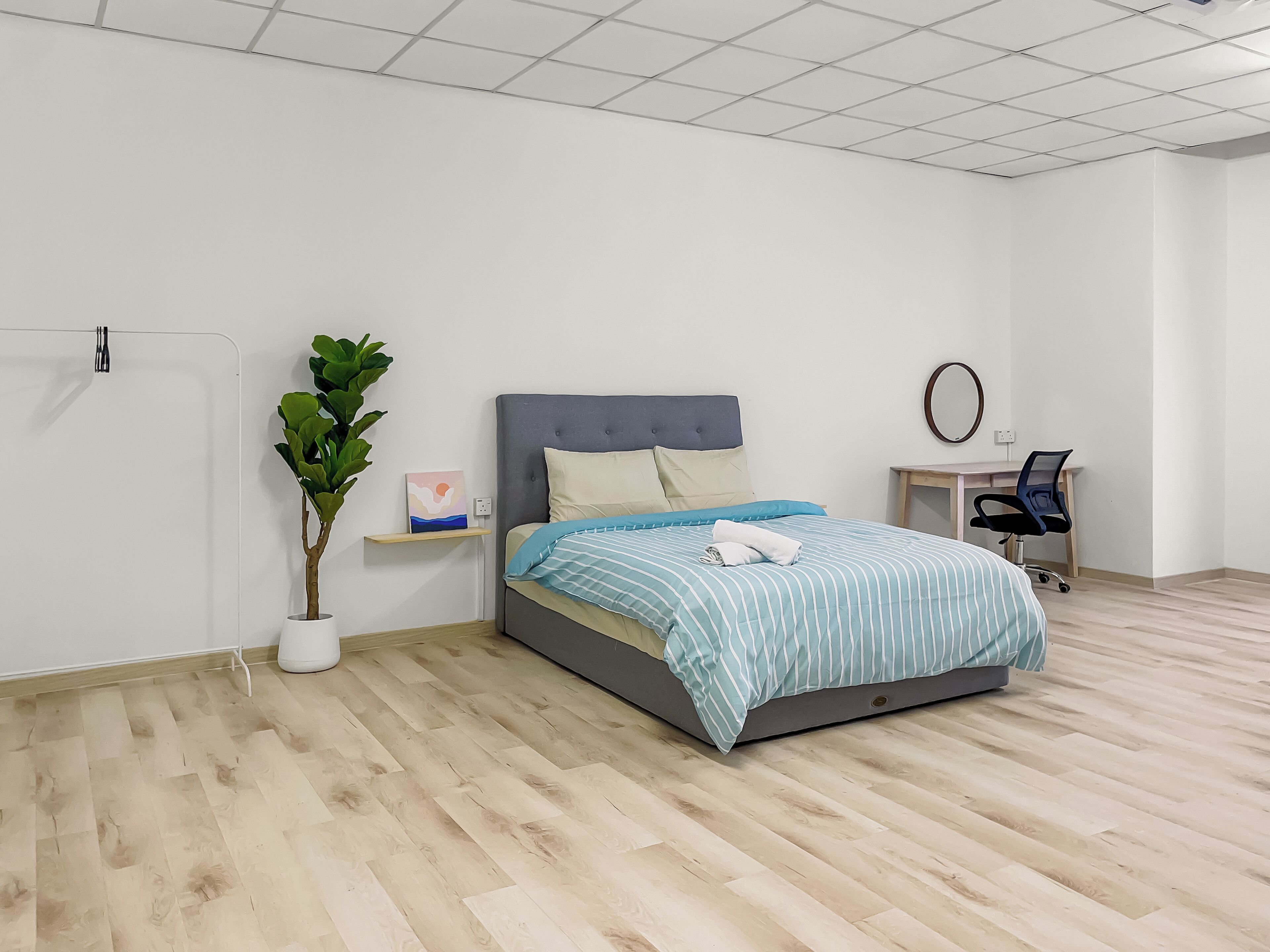 Un dormitorio con cama, escritorio, silla, planta en maceta y espejo montado en la pared.