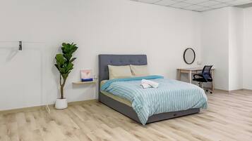 Un dormitorio con cama, escritorio, silla, planta en maceta y espejo montado en la pared.