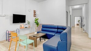 A modern living room with a blue sectional sofa, a wooden coffee table, and a TV mounted on the wall. - 3 Bedroom  (Batu Pahat)