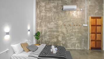A hotel room with a bed, bedside lamps, an air conditioning unit, a wooden door, and a potted plant.