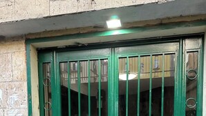 A green metal gate with vertical bars and two handles, leading to a tiled entrance. - Napoli Historic center Tribunali Duomo house (Napoli)