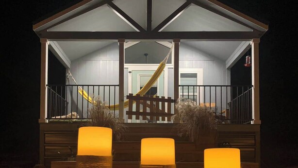 A covered outdoor area with a wooden deck, a yellow slide, and three lit candles on the ground. - Monte Mahala – Two Unique Homes! (Johnson City)