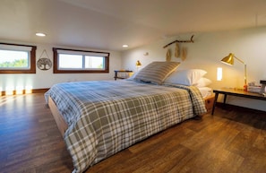Quarto com uma cama grande, duas mesas de cabeceira, um criado-mudo, uma janela e uma luminária fixada na parede.