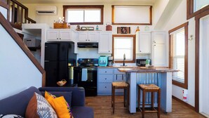 A compact kitchen with white cabinets, a black refrigerator, and a small island with stools. - Monte Mahala – Two Unique Homes! (Johnson City)