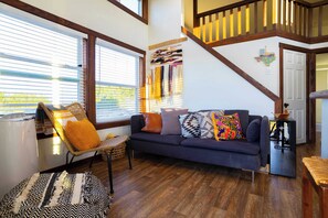 A cozy living room with a dark blue sofa, a wicker chair, and a patterned rug. - Monte Mahala – Two Unique Homes! (Johnson City)