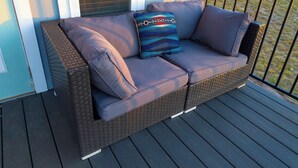 A wicker sofa with cushions on a wooden deck. - Monte Mahala – Two Unique Homes! (Johnson City)