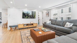 A modern living room with a grey sofa, wooden side table, and a large flat-screen TV mounted on the wall.