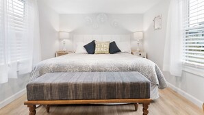 A bedroom with a large bed, two bedside tables, a bench, and a wall with decorative elements.