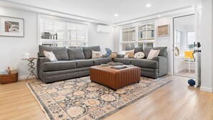 A modern living room with a grey sectional sofa, a brown ottoman, and a patterned rug.