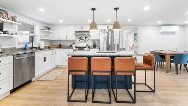 A modern kitchen with white cabinets, a central island, and a dining area with chairs.