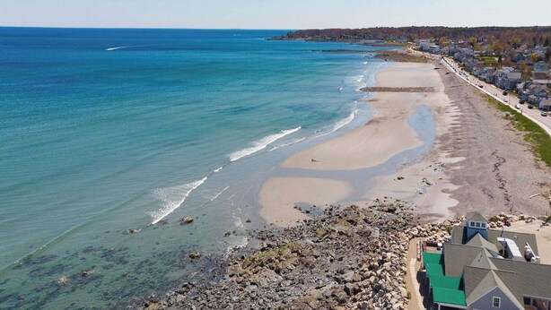 Ein Küstenort mit sandigem Strand, klarem, blauem Wasser und Häusern entlang der Küste.