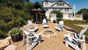 Eine Terrasse mit Adirondack-Stühlen, einer Feuerstelle und einem Holzkiosk.