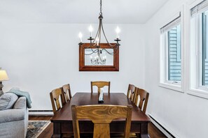 A dining room with a wooden table and chairs, a chandelier, and a framed mirror on the wall.