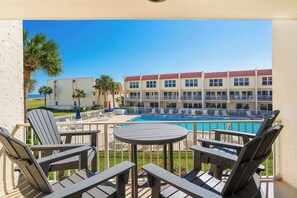 A poolside area with lounge chairs and a table, a building with a red roof, and a clear blue sky. - Pier Point South Ocean View Condo B-18 (St. Augustine)