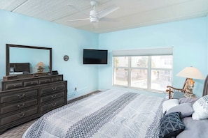 Una camera da letto con un letto, una cassettiera, una TV, una finestra e una ventola a soffitto.