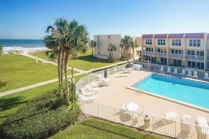A hotel with a pool, lounge chairs, and a view of the ocean.