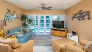 A living room with a blue sofa, beige armchairs, a TV, and a ceiling fan.