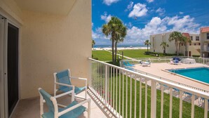 A balcony with a pool, chairs, and a view of the beach and ocean.