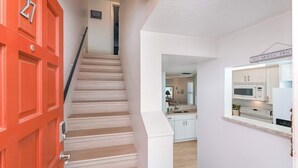 Una escalera conduce a una cocina con armarios blancos y una puerta roja con el número 27.