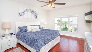 Une chambre à coucher avec un lit, un ventilateur de plafond, une fenêtre donnant sur un beau paysage et une table de chevet avec une lampe.