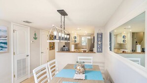Un espace repas comprenant une table, des chaises, un luminaire suspendu et un panneau fixé au mur.