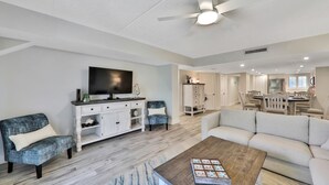 A living room with a TV, two armchairs, a sofa, a coffee table, and a ceiling fan. - Pier Point South Ocean View Condo D-44 (St. Augustine)