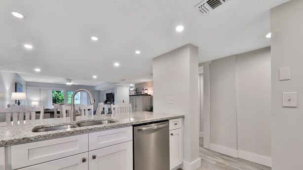 A modern kitchen with white cabinetry, a stainless steel dishwasher, and a granite countertop. - Pier Point South Ocean View Condo D-44 (St. Augustine)